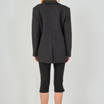 Back view of a black tailored blazer featuring a center back seam and a fitted silhouette, paired with fitted black capri pants.