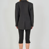 Back view of a black tailored blazer featuring a center back seam and a fitted silhouette, paired with fitted black capri pants.