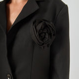 Close-up view of a black blazer highlighting the notch lapel, large intricate 3D rose appliqué, and textured fabric.
