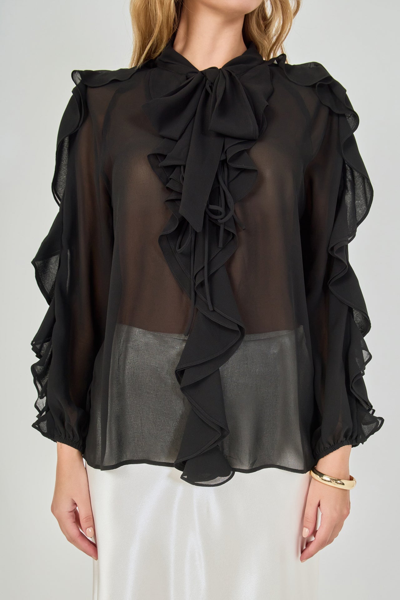 Close-up view of black sheer ruffled blouse highlighting the tie-neck bow, delicate front ruffles, and lightweight sheer chiffon fabric.