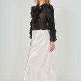 Side view of black sheer ruffled blouse featuring long sleeves with cascading outer ruffles, paired with a fluid cream satin midi skirt.