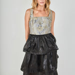Mid-shot face-forward posed view of a mixed-media midi dress showcasing the grey and gold floral jacquard square-neck bodice and voluminous black tiered skirt.