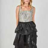 Mid-shot face-forward posed view of a mixed-media midi dress showcasing the grey and gold floral jacquard square-neck bodice and voluminous black tiered skirt.