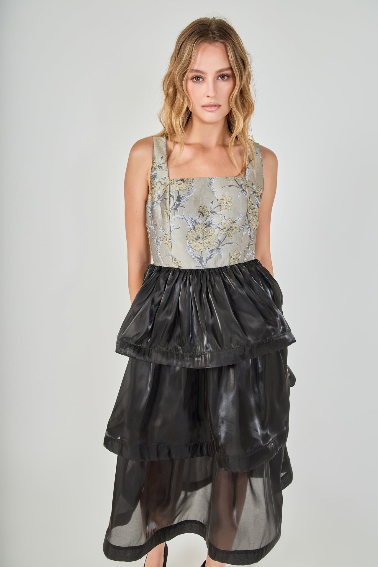 Mid-shot face-forward posed view of a mixed-media midi dress showcasing the grey and gold floral jacquard square-neck bodice and voluminous black tiered skirt.