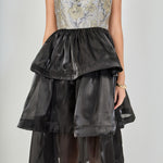 Close-up view of the dress bodice featuring a square neckline, structured bust seams, grey and gold metallic floral jacquard fabric, and a gathered black skirt waistband.