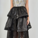 Close-up view of the dress bodice featuring a square neckline, structured bust seams, grey and gold metallic floral jacquard fabric, and a gathered black skirt waistband.