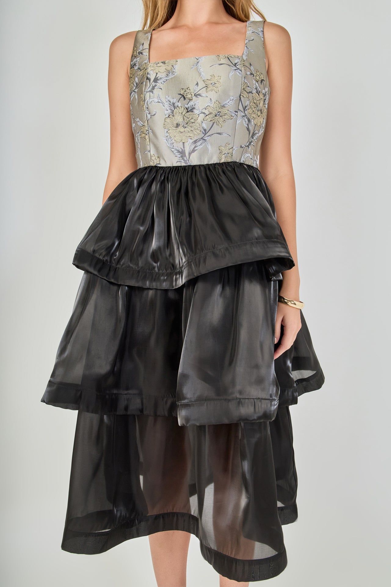 Close-up view of the dress bodice featuring a square neckline, structured bust seams, grey and gold metallic floral jacquard fabric, and a gathered black skirt waistband.