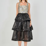 Full-length front view of a mixed-media midi dress featuring a grey and gold floral jacquard sleeveless bodice with a square neckline, paired with a voluminous black tiered organza skirt.