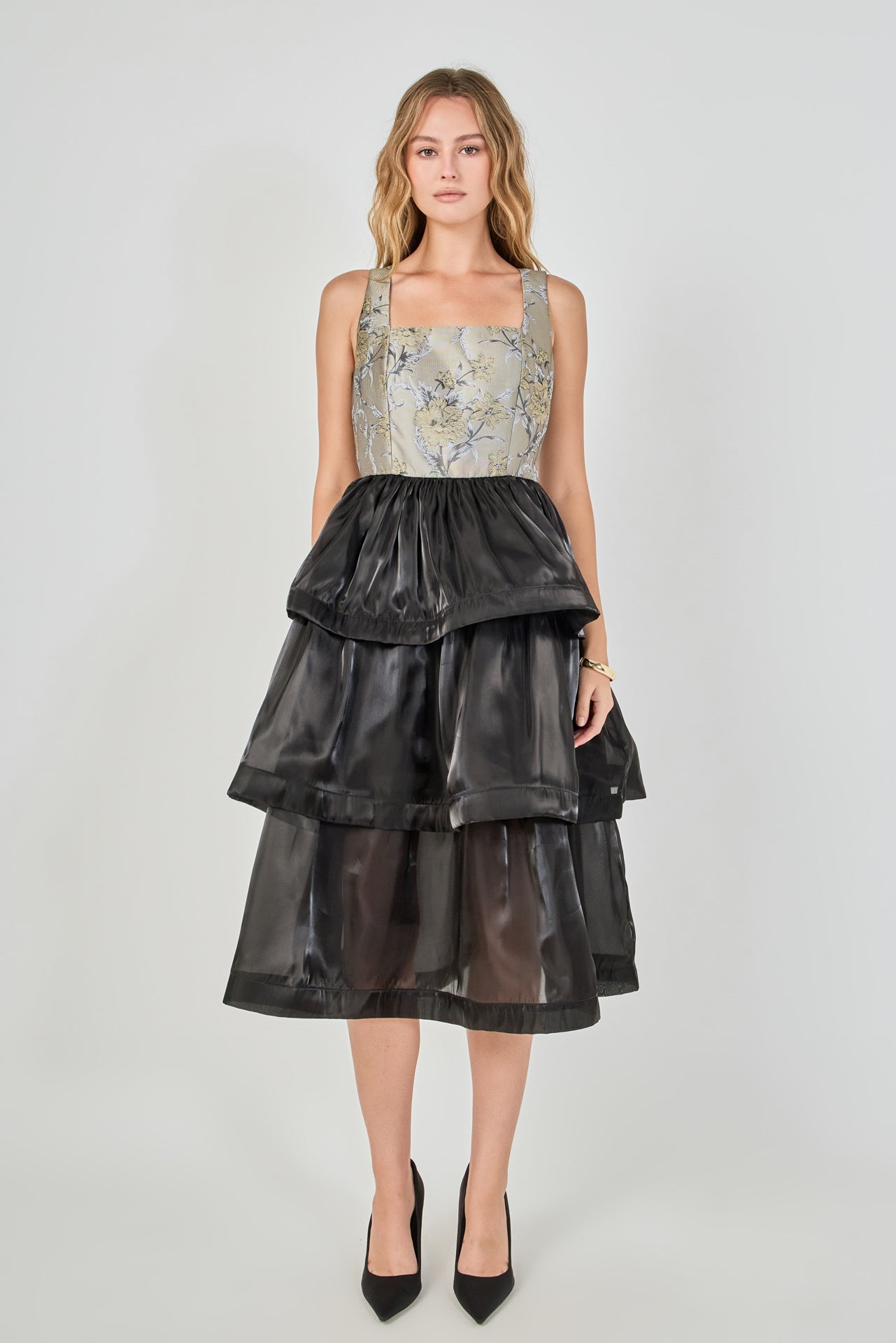 Full-length front view of a mixed-media midi dress featuring a grey and gold floral jacquard sleeveless bodice with a square neckline, paired with a voluminous black tiered organza skirt.