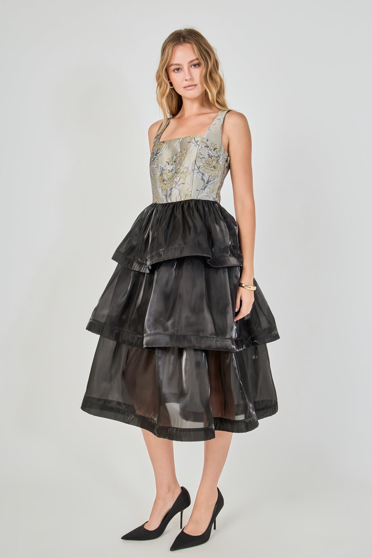 Side view of a mixed-media midi dress featuring a fitted floral jacquard bodice and a voluminous black tiered organza skirt.