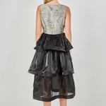 Back view of a mixed-media midi dress featuring a square back neckline, fitted floral jacquard bodice, and a three-tiered black organza midi skirt.