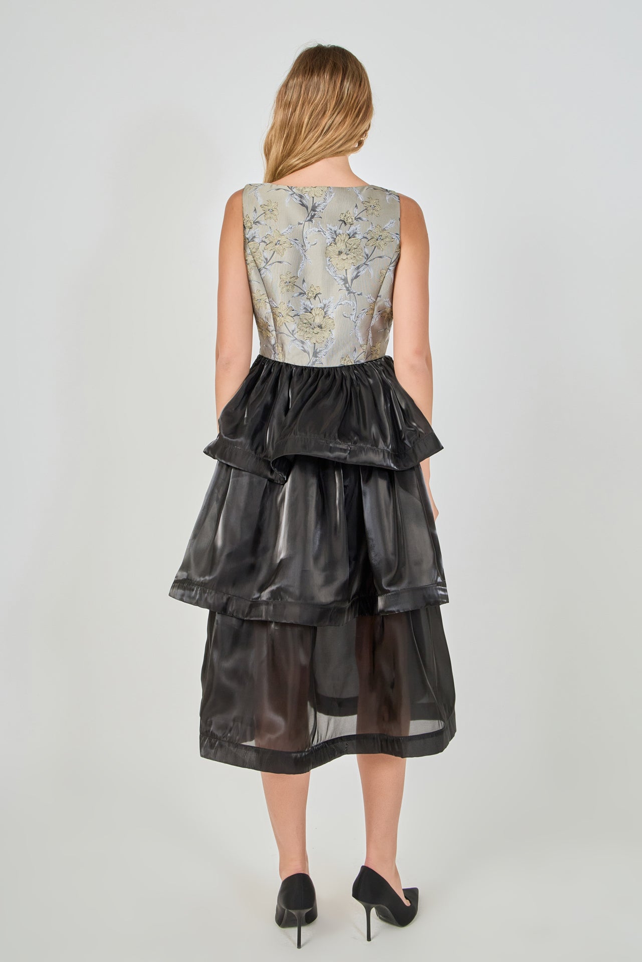 Back view of a mixed-media midi dress featuring a square back neckline, fitted floral jacquard bodice, and a three-tiered black organza midi skirt.