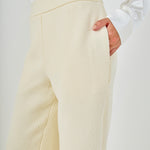 Close-up view of cream high-waisted tweed trousers highlighting the flat waistband, textured weave, and side slant pocket detail.