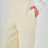 Close-up view of cream high-waisted tweed trousers highlighting the flat waistband, textured weave, and side slant pocket detail.
