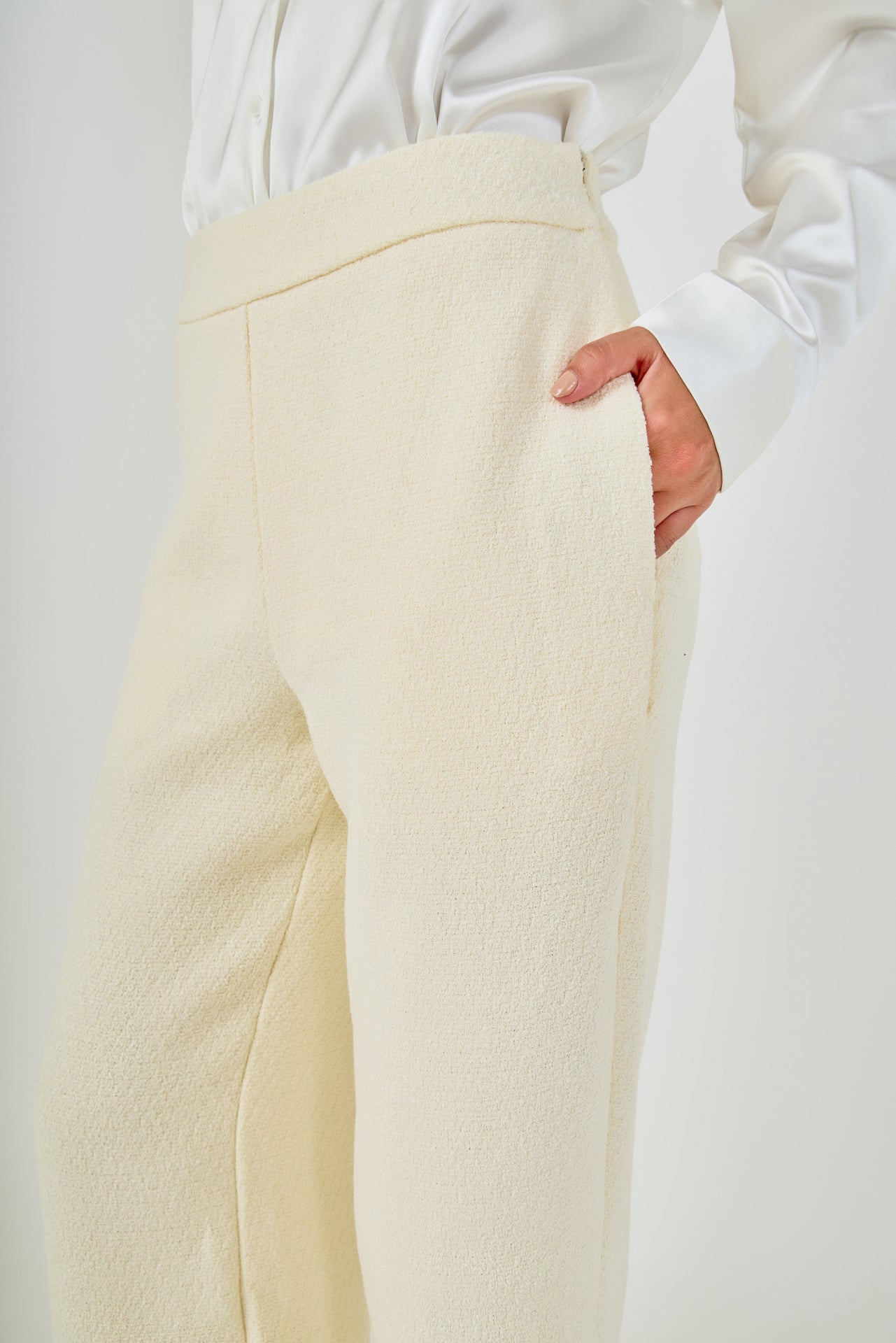 Close-up view of cream high-waisted tweed trousers highlighting the flat waistband, textured weave, and side slant pocket detail.