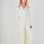 Face-forward posed view of cream high-waisted wide-leg tweed trousers styled with a long-sleeve white satin button-down shirt.
