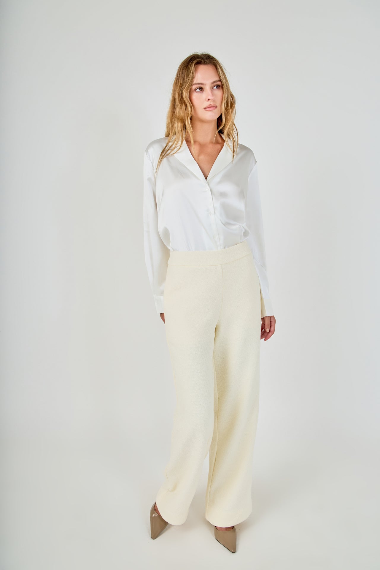 Face-forward posed view of cream high-waisted wide-leg tweed trousers styled with a long-sleeve white satin button-down shirt.