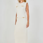 Side profile view of cream sleeveless knit maxi dress displaying the straight drape and structured cap shoulder design.