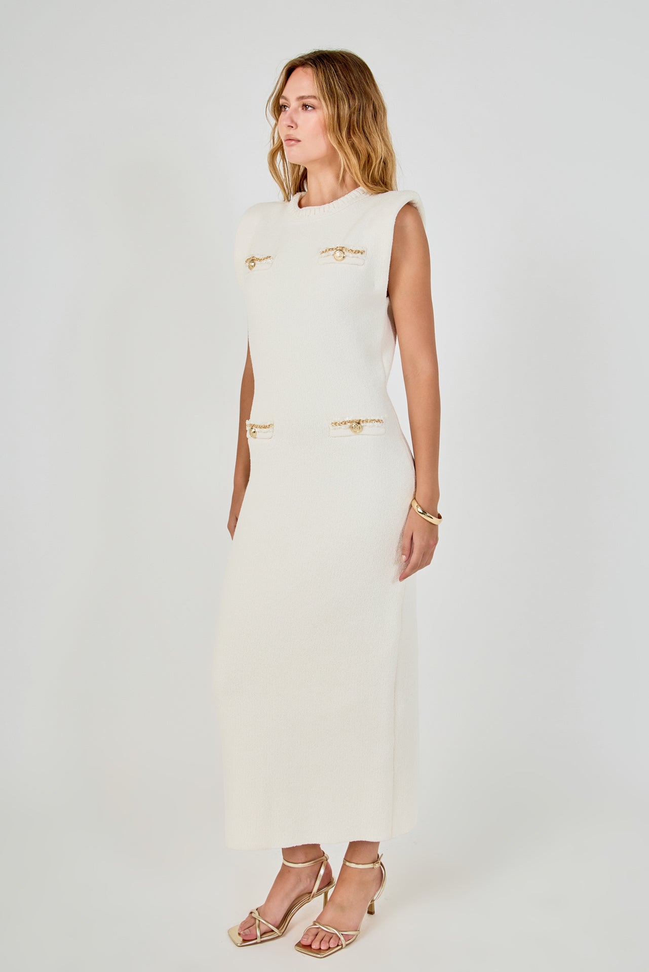 Side profile view of cream sleeveless knit maxi dress displaying the straight drape and structured cap shoulder design.