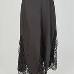 Ultra close-up detail view of a black skirt showcasing smooth, solid black fabric flanked by sheer black floral lace panels, highlighting intricate floral embroidery, sheer mesh netting, angled seam construction, and delicate scalloped eyelash lace trim.