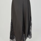 Ultra close-up detail view of a black skirt showcasing smooth, solid black fabric flanked by sheer black floral lace panels, highlighting intricate floral embroidery, sheer mesh netting, angled seam construction, and delicate scalloped eyelash lace trim.