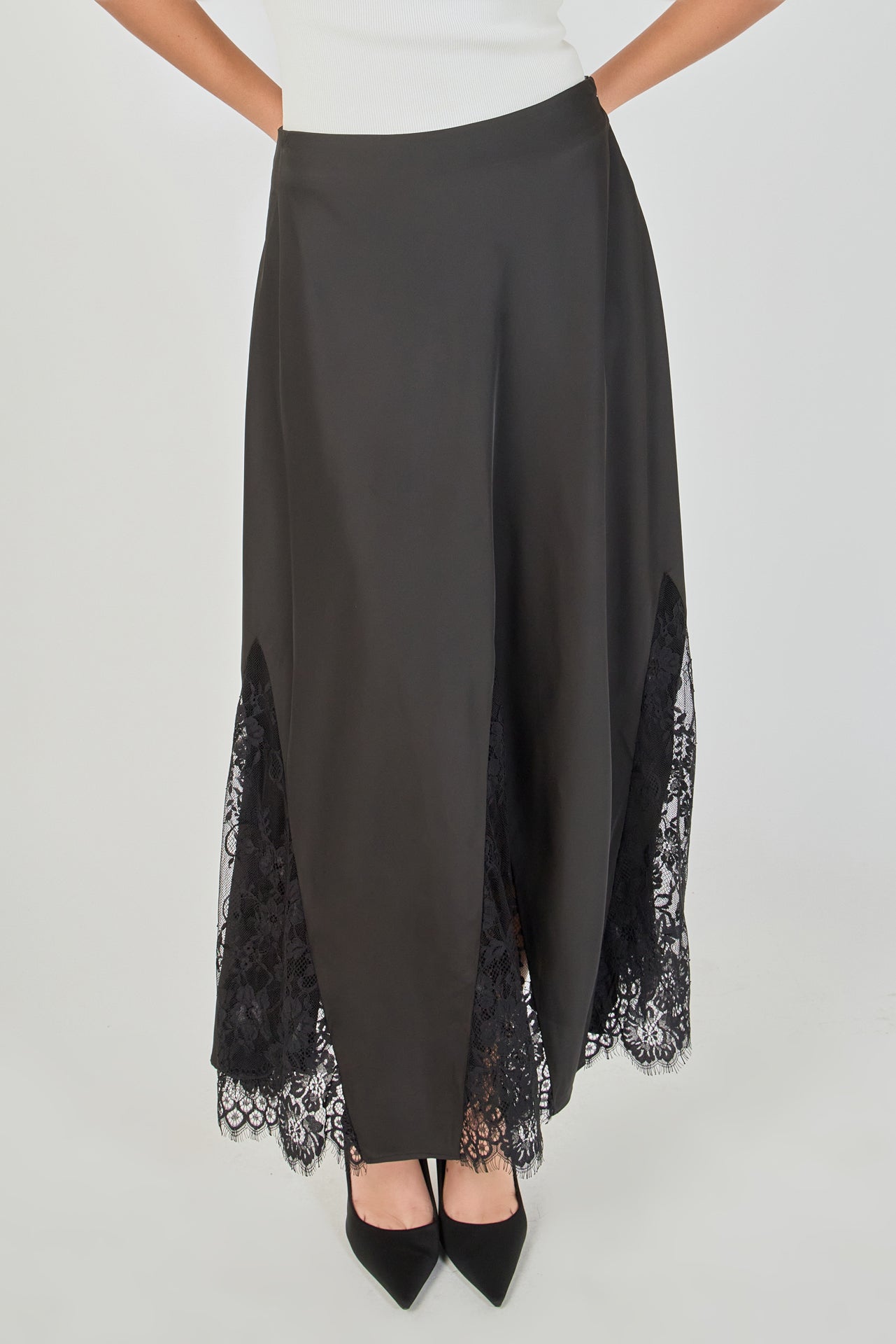Ultra close-up detail view of a black skirt showcasing smooth, solid black fabric flanked by sheer black floral lace panels, highlighting intricate floral embroidery, sheer mesh netting, angled seam construction, and delicate scalloped eyelash lace trim.