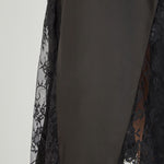 Close-up view of black maxi skirt highlighting the high waistline, fluid drape, and sheer floral eyelash lace paneling at the lower hem.