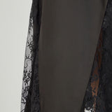 Close-up view of black maxi skirt highlighting the high waistline, fluid drape, and sheer floral eyelash lace paneling at the lower hem.