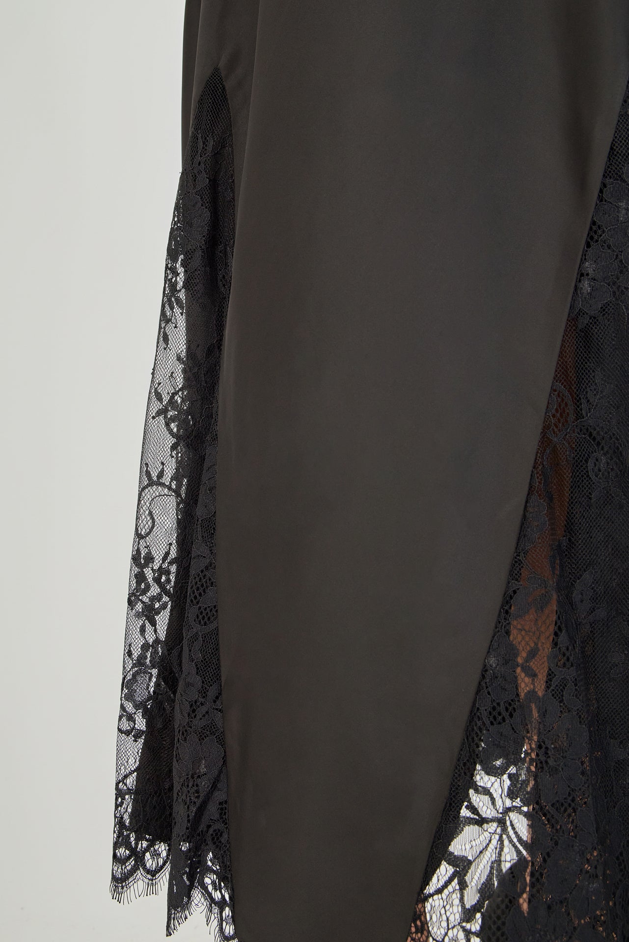 Close-up view of black maxi skirt highlighting the high waistline, fluid drape, and sheer floral eyelash lace paneling at the lower hem.