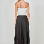 Back view of black maxi skirt featuring a smooth high waistband and sheer black lace godet panels along the hemline.