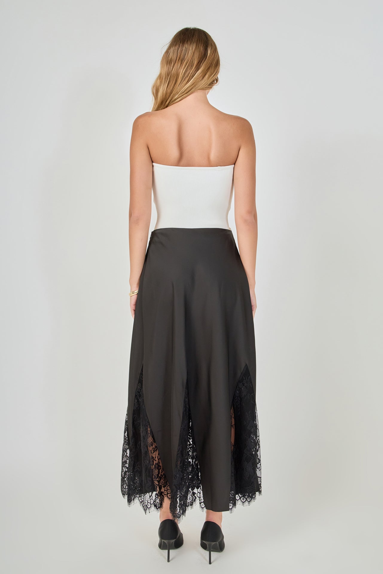 Back view of black maxi skirt featuring a smooth high waistband and sheer black lace godet panels along the hemline.