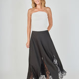 Mid-shot face-forward posed view of black maxi skirt featuring lace hem panels, with the model posing with hands resting on her hips to emphasize the waistline and lower lace detailing.