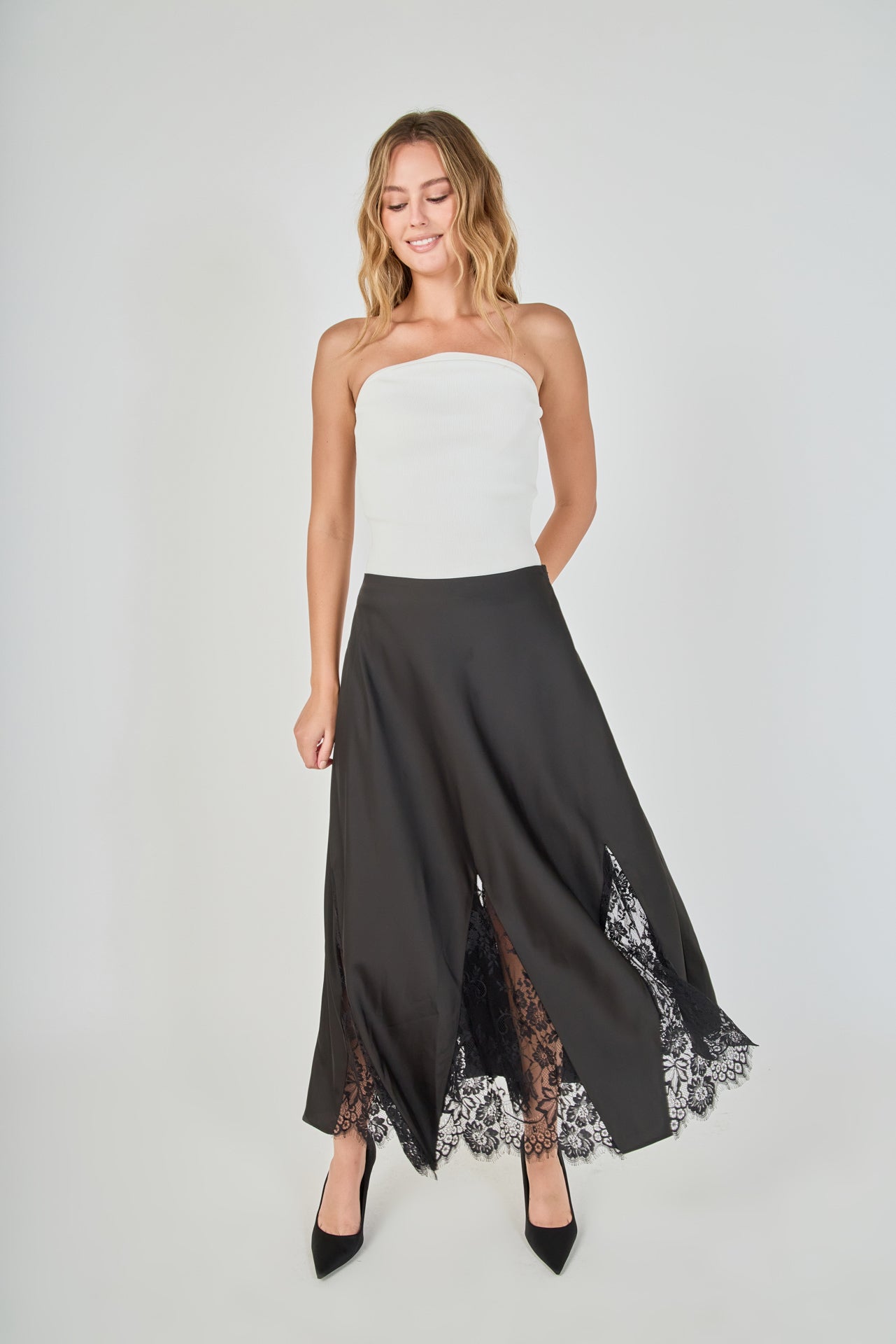 Mid-shot face-forward posed view of black maxi skirt featuring lace hem panels, with the model posing with hands resting on her hips to emphasize the waistline and lower lace detailing.