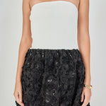 Close-up view of a strapless mixed-media mini dress highlighting the white ribbed knit bodice and the textured black 3D floral rosette skirt with subtle sequin accents.