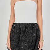 Close-up view of a strapless mixed-media mini dress highlighting the white ribbed knit bodice and the textured black 3D floral rosette skirt with subtle sequin accents.