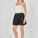Side view of a strapless mixed-media mini dress showcasing the fitted white bodice and the voluminous black 3D rosette bubble skirt.
