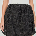 Mid-shot face-forward posed view of a strapless mixed-media mini dress showcasing the white ribbed top and textured black rosette bubble skirt.