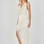 Side profile view of a champagne satin halter dress showcasing the draped cowl front and sweeping asymmetrical lace hemline.