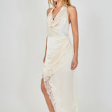 Side profile view of a champagne satin halter dress showcasing the draped cowl front and sweeping asymmetrical lace hemline.