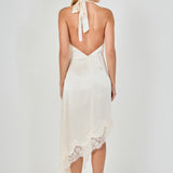 Straight-on back view of a champagne satin dress displaying a self-tie halter neck, open low back, and asymmetrical lace skirt hem.