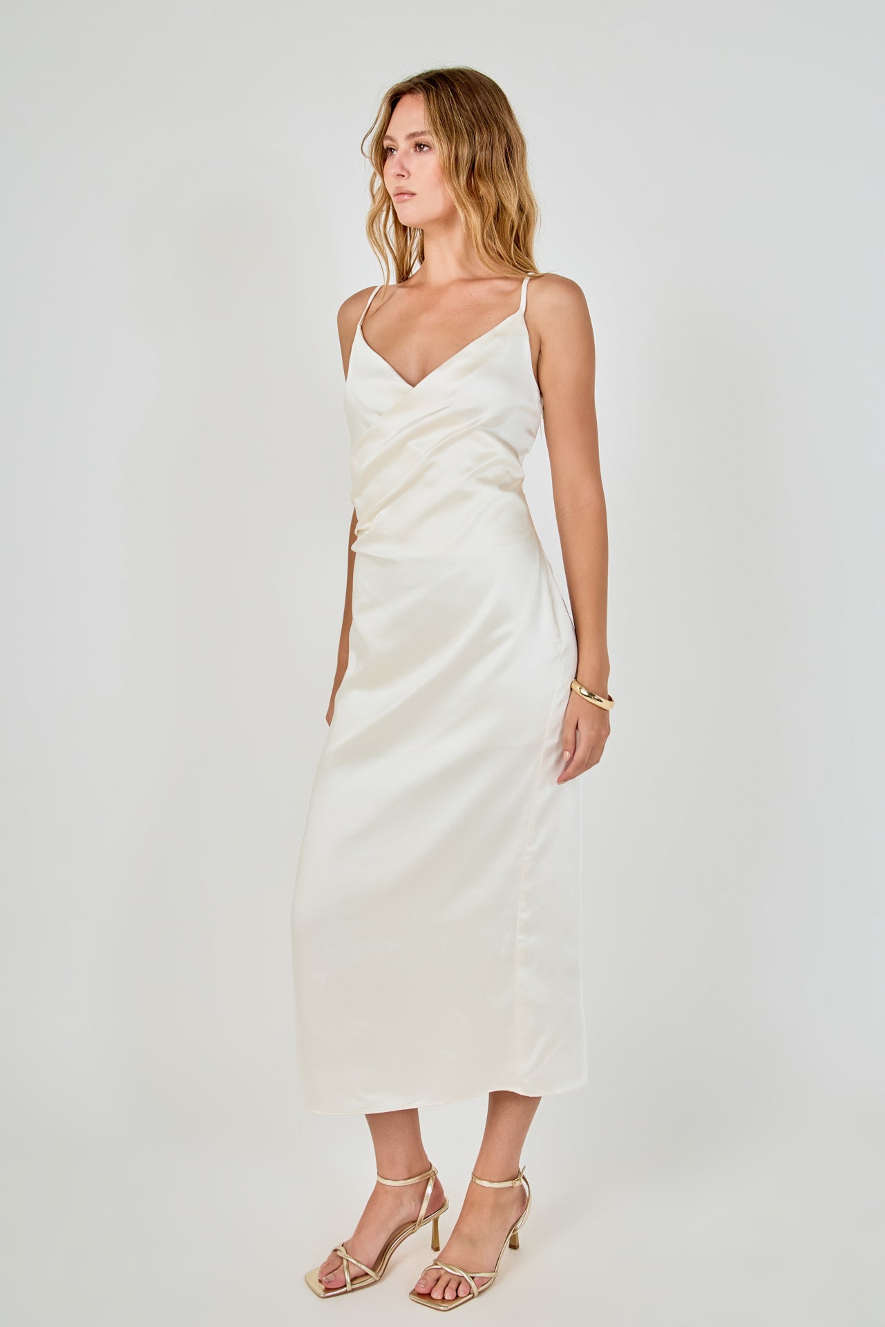 Side profile view of a champagne satin wrap midi dress displaying the slim-fitting drape and discreet side zipper detail.