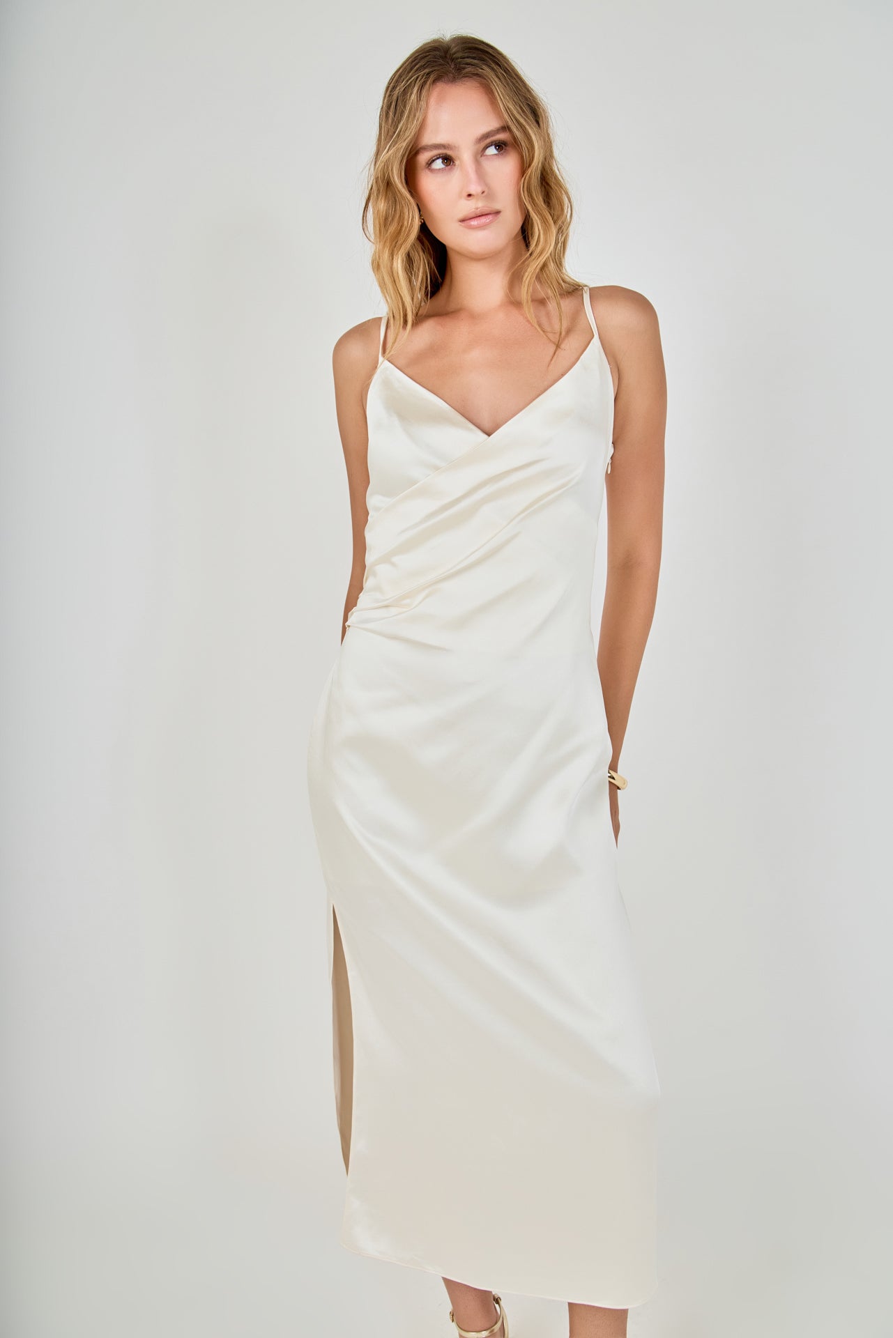 Face-forward posed view of a champagne satin wrap midi dress featuring a draped wrap neckline, subtle side ruching, and slender adjustable straps.