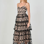 Side view of a black floral embroidered tiered midi dress featuring a fitted sleeveless bodice, contrast beige lining, and a fluid tiered skirt silhouette.