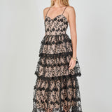 Side view of a black floral embroidered tiered midi dress featuring a fitted sleeveless bodice, contrast beige lining, and a fluid tiered skirt silhouette.