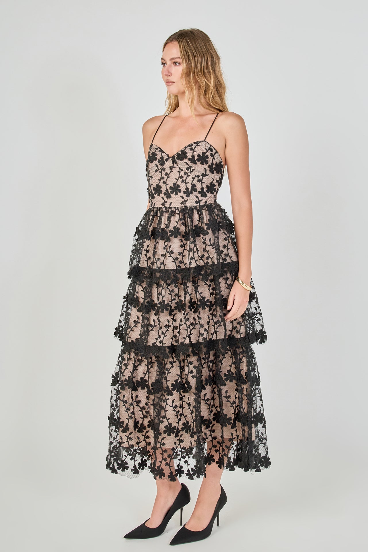 Side view of a black floral embroidered tiered midi dress featuring a fitted sleeveless bodice, contrast beige lining, and a fluid tiered skirt silhouette.