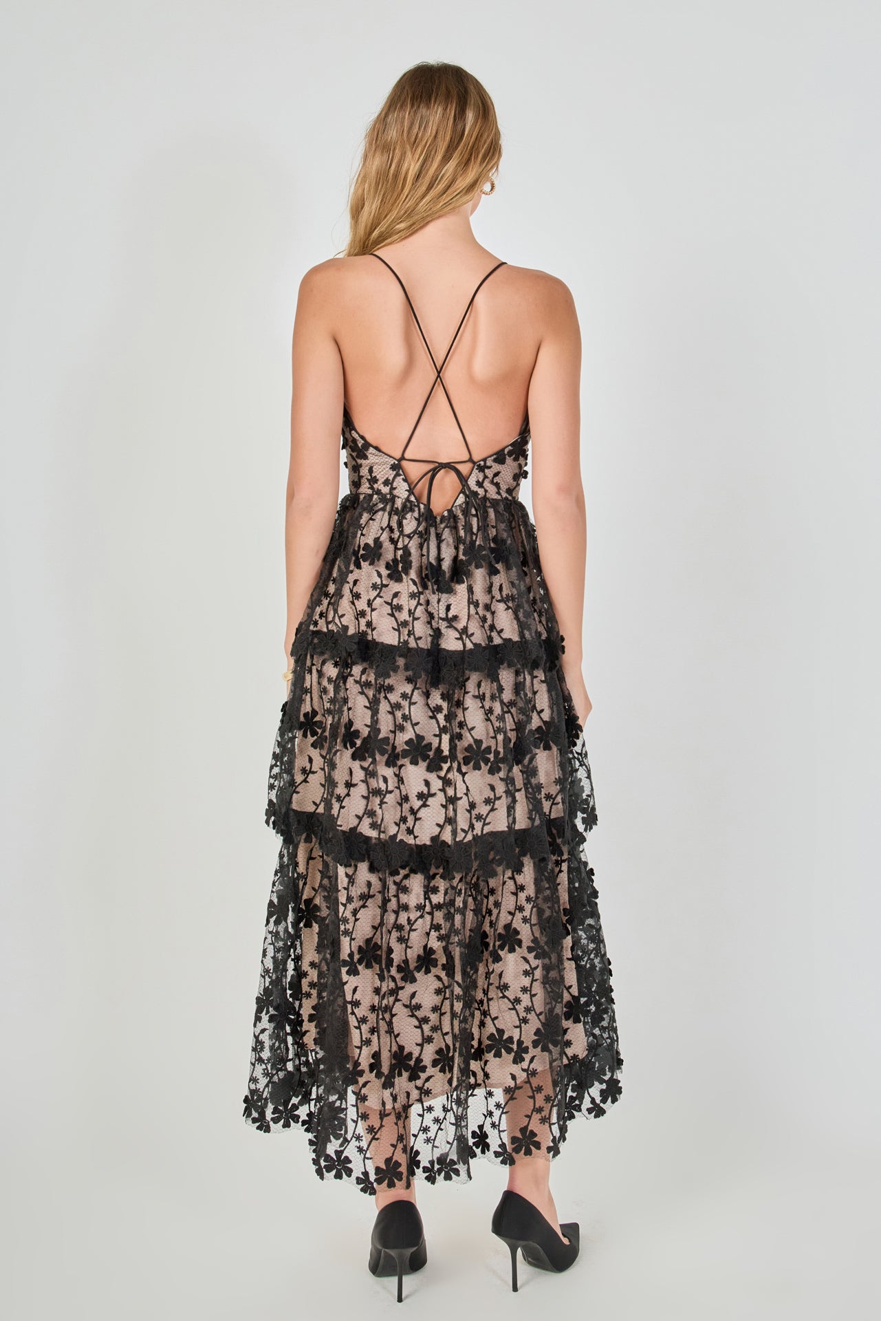 Back view of a black floral embroidered tiered midi dress featuring thin spaghetti straps, a straight back neckline, and a multi-tiered ruffled midi hem.