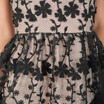 Ultra close-up detail view of sheer black mesh fabric featuring intricate raised black floral embroidery and vine motifs layered over a contrast beige lining.