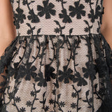 Ultra close-up detail view of sheer black mesh fabric featuring intricate raised black floral embroidery and vine motifs layered over a contrast beige lining.