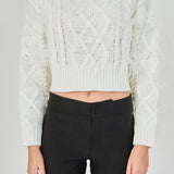 Mid-shot view of cream long-sleeve cable-knit sweater focusing on the crew neckline, wide ribbed cropped hem, and feather detailing.