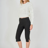 Side profile view of cream cropped cable-knit sweater displaying the long sleeve drape, wispy feather trim, and fitted waistline.